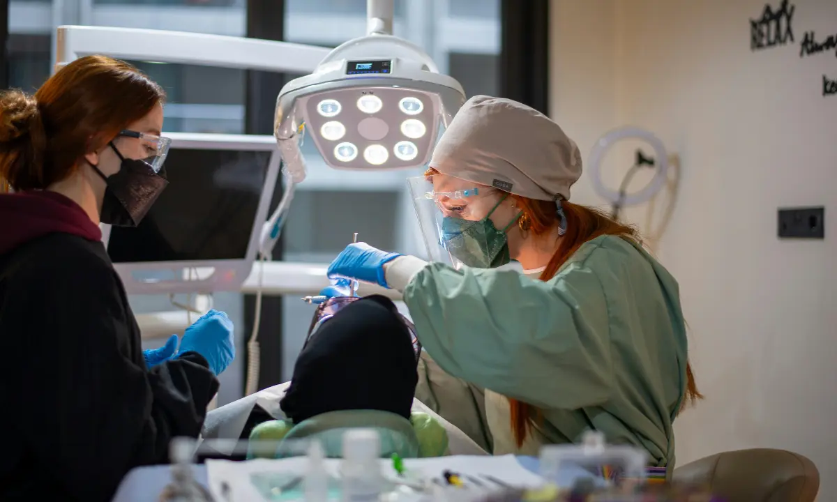 Two dental clinicians in masks, gloves and face shields treating a patient under an overhead dental light