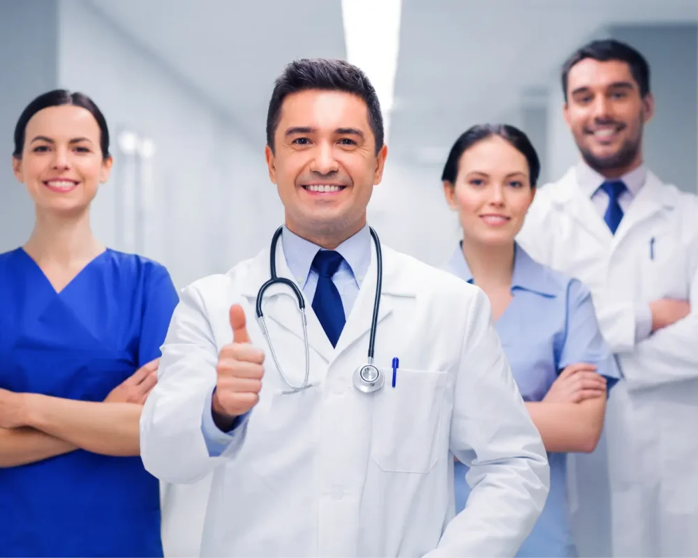Diverse medical team celebrating successful billing outcomes - one male doctor giving thumbs up with two female and one male colleagues smiling in modern clinic office